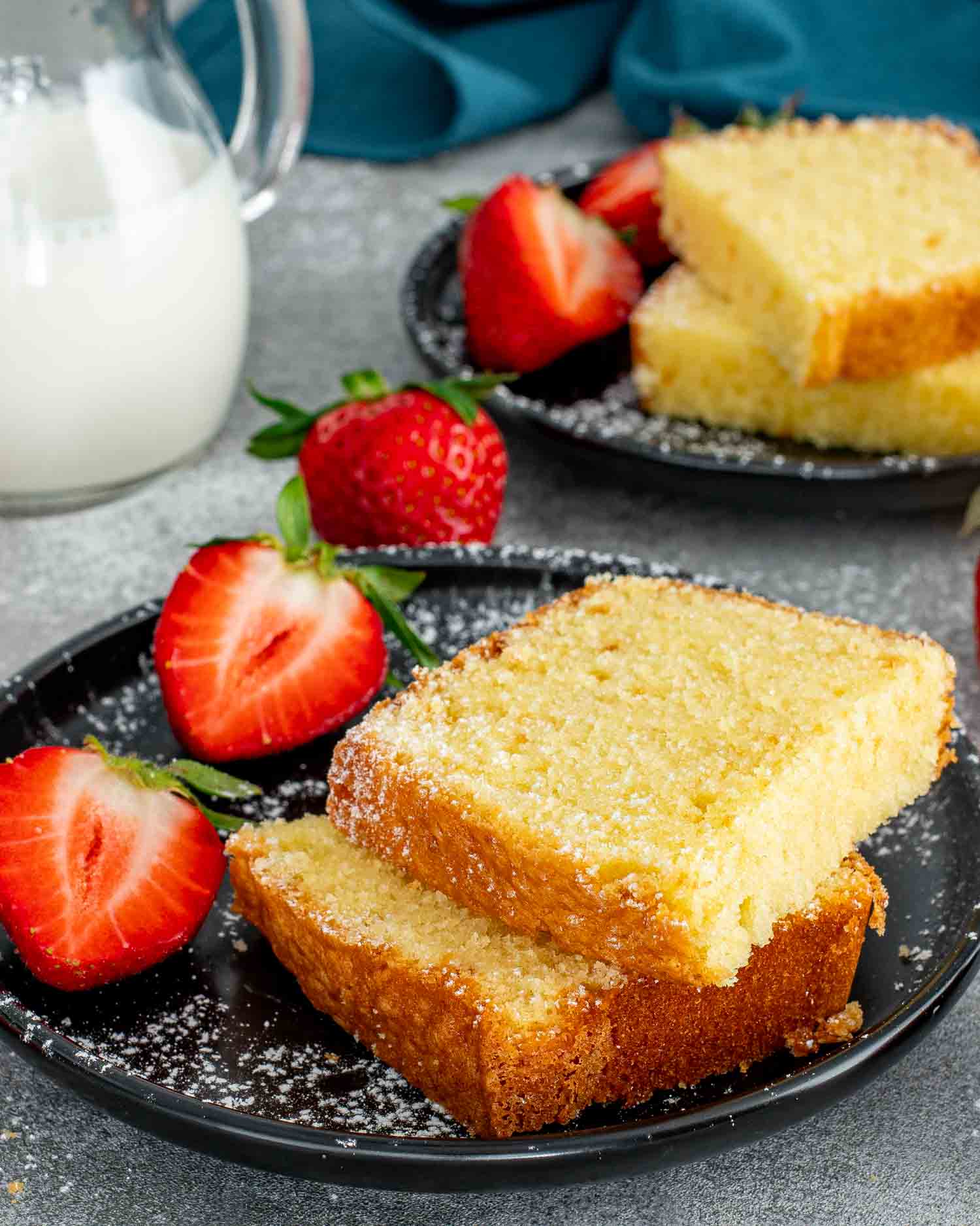 a couple slices of freshly baked butter cake along side a couple strawberries on a black plate.