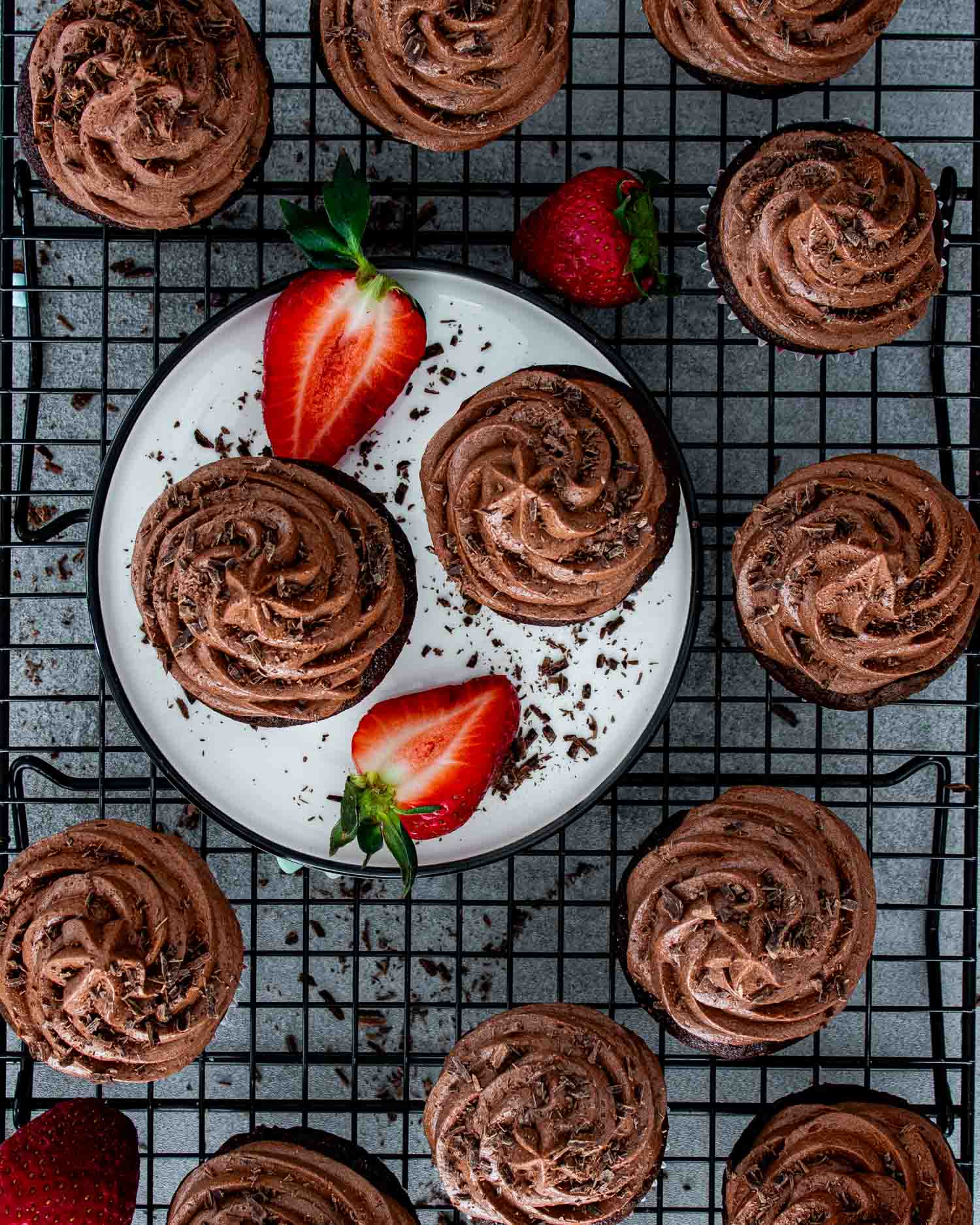chocolate cupcakes on a cooling rack with white plate in the middle.