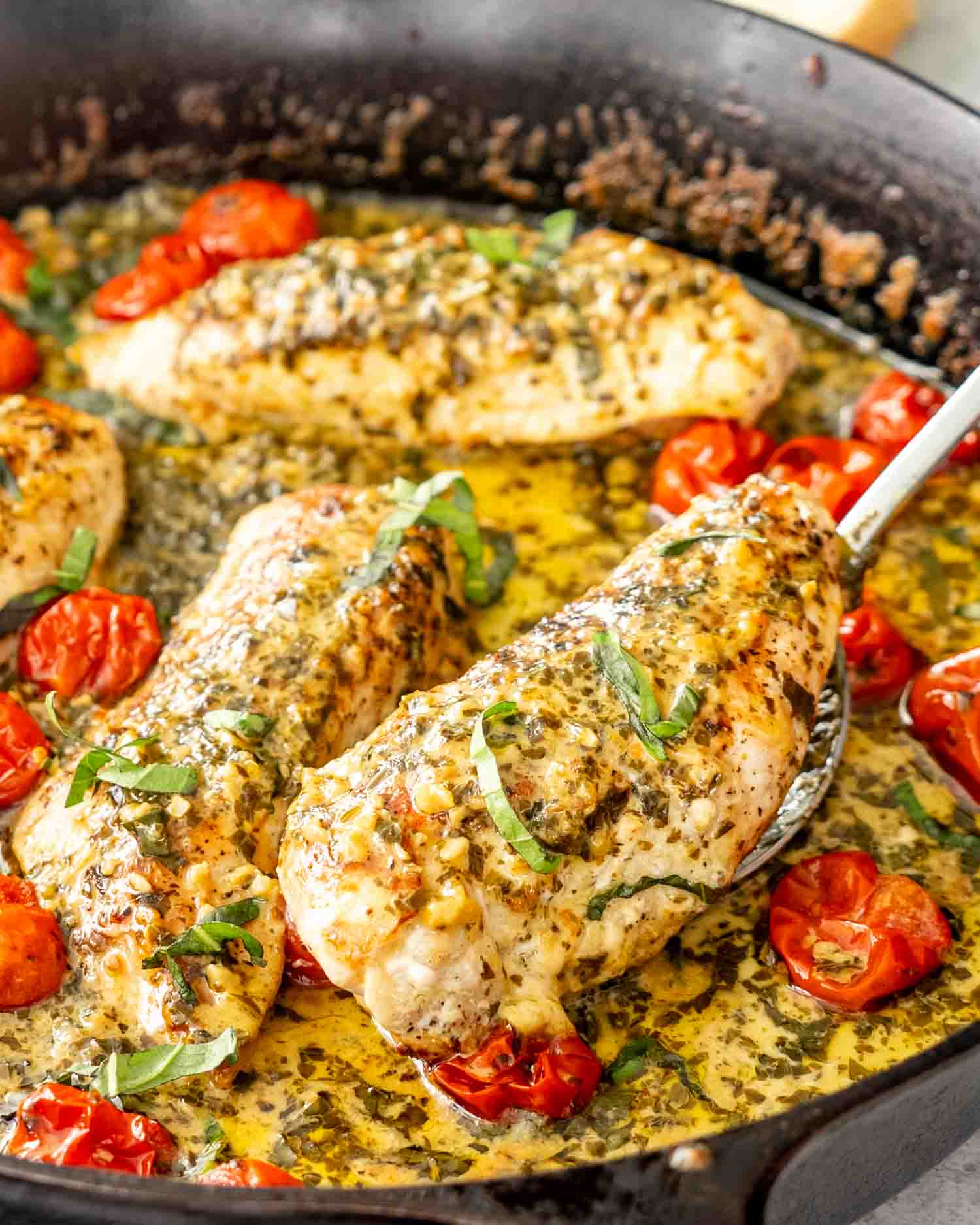 a spoon holding a creamy pesto chicken breast inside a cast iron skillet.