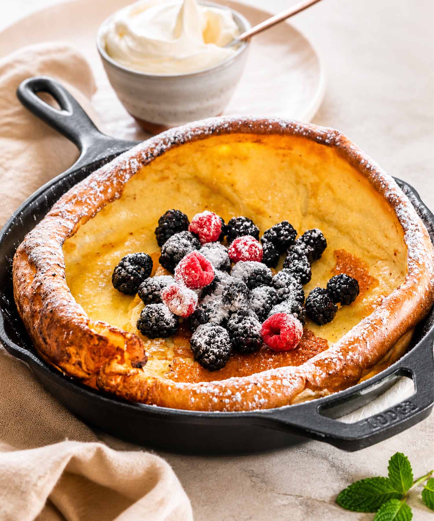 A homemade Dutch baby pancake with crispy edges and a custardy center served in a traditional black cast iron pan.