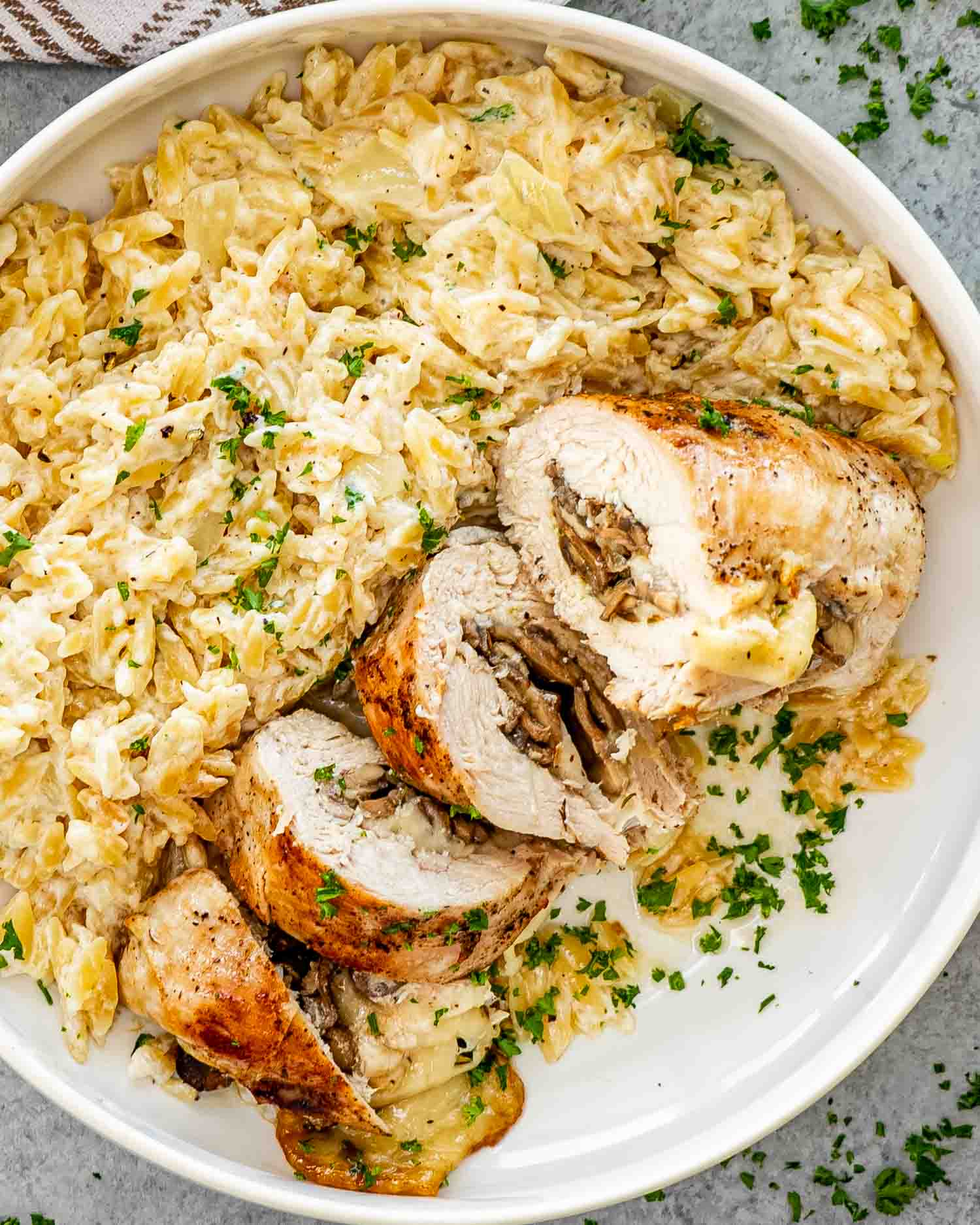 a mushroom stuffed chicken breast along some parmesan orzo in a white bowl.