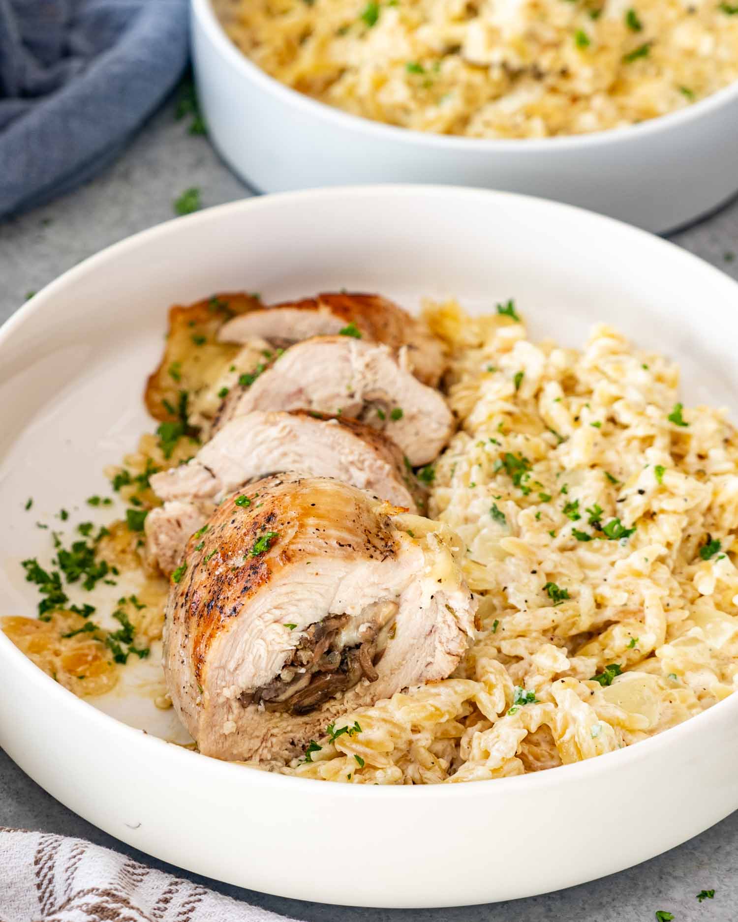 a mushroom stuffed chicken breast along some parmesan orzo in a white bowl.