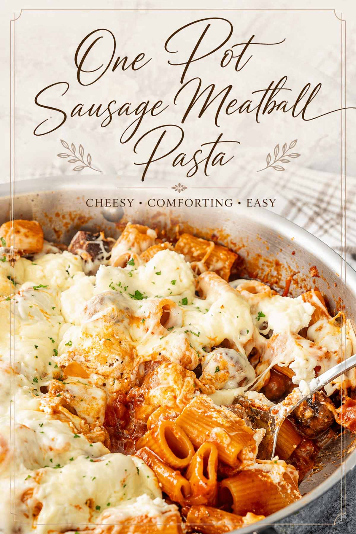 Vertical view of cheesy sausage meatball pasta with a spoon lifting a serving of rigatoni and melted cheese.