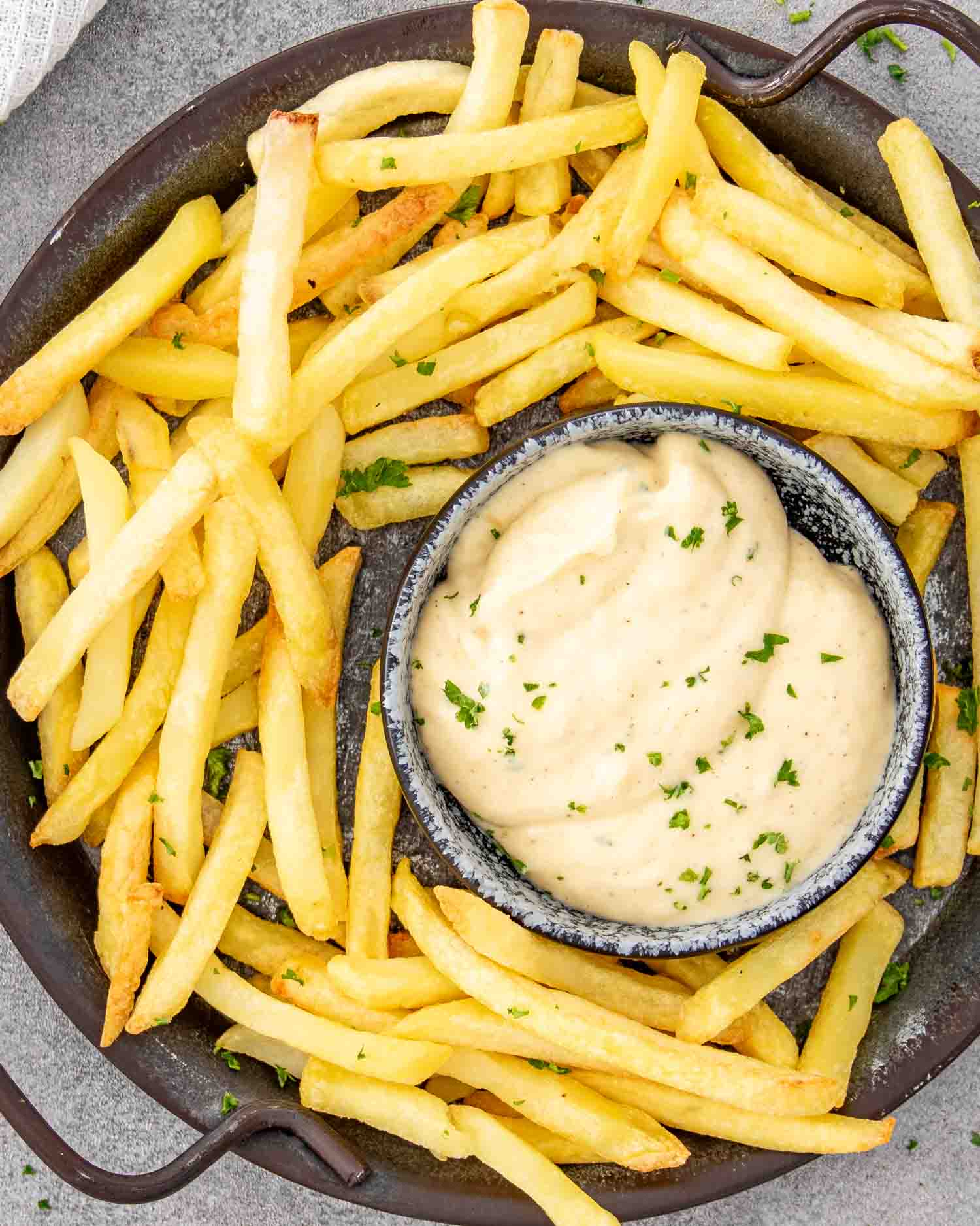 roasted garlic aioli in a little bowl surrounded by french fries on a plate.