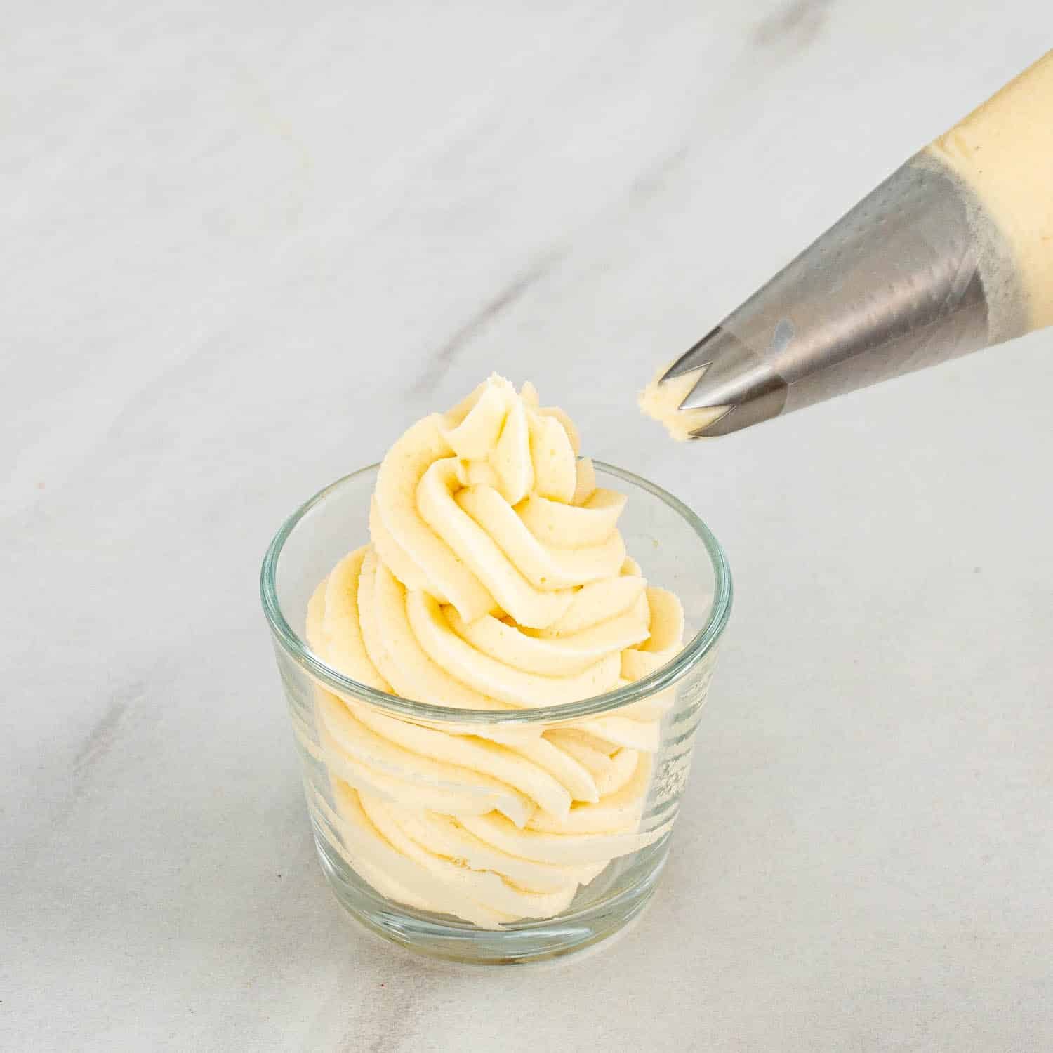 piping vanilla frosting in a glass.
