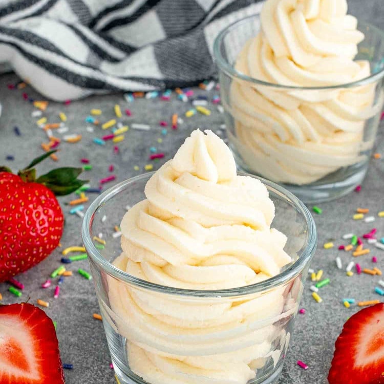 vanilla frosting in 2 glasses with some strawberries around.