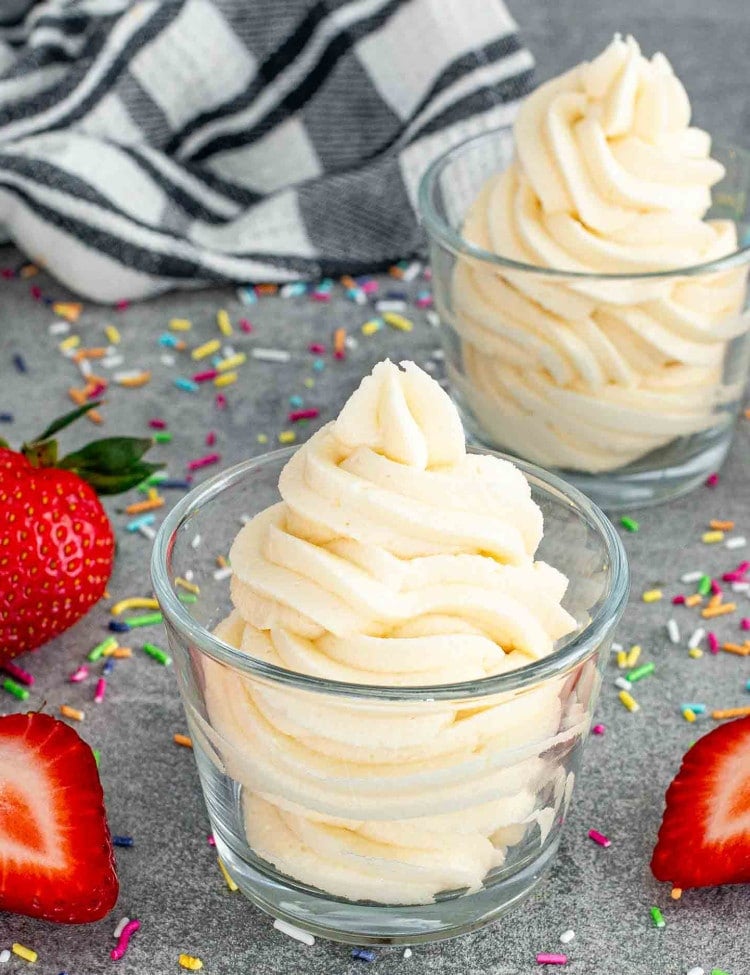 vanilla frosting in 2 glasses with some strawberries around.
