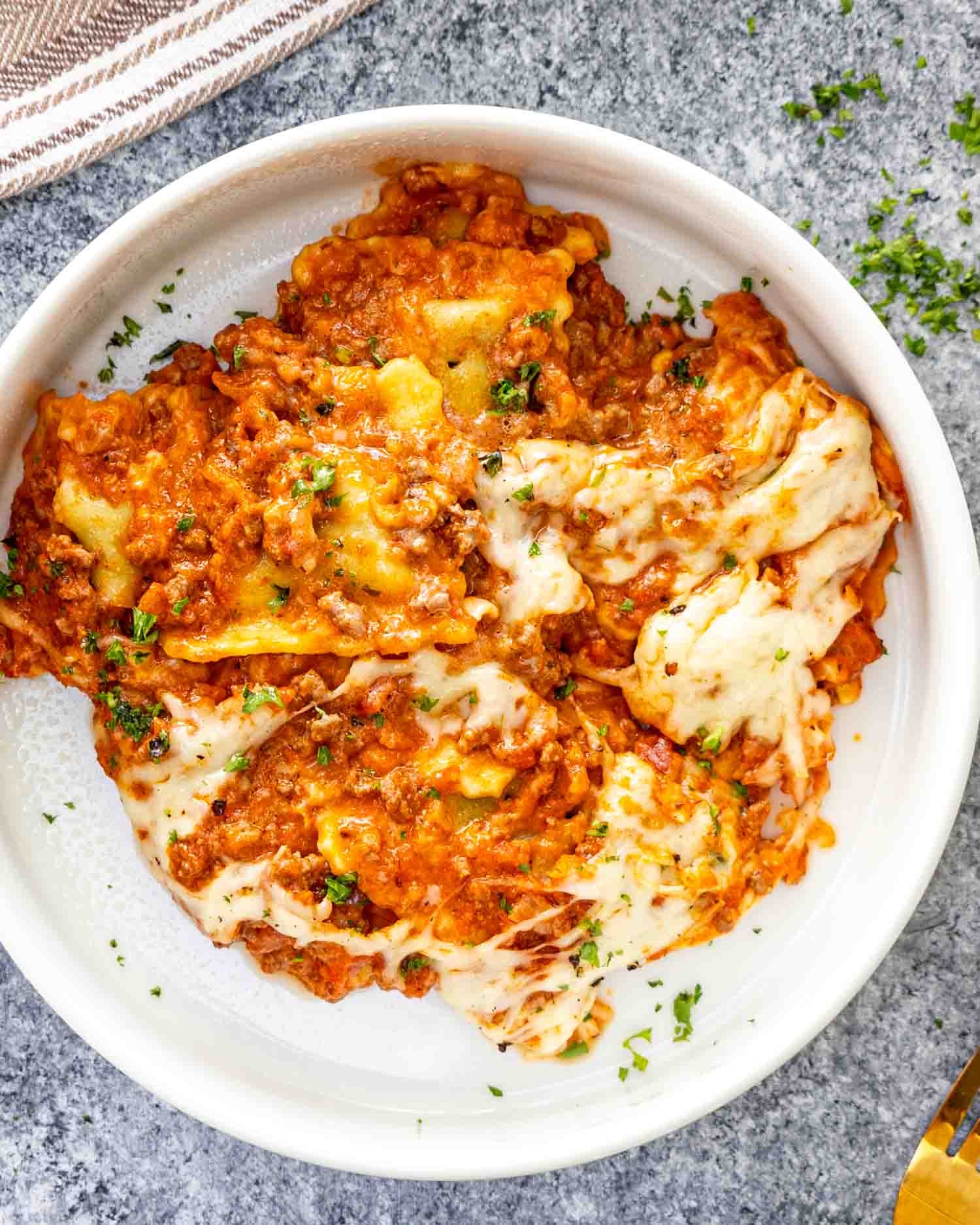 a serving of baked ravioli in a white bowl garnished with a bit of parsley.