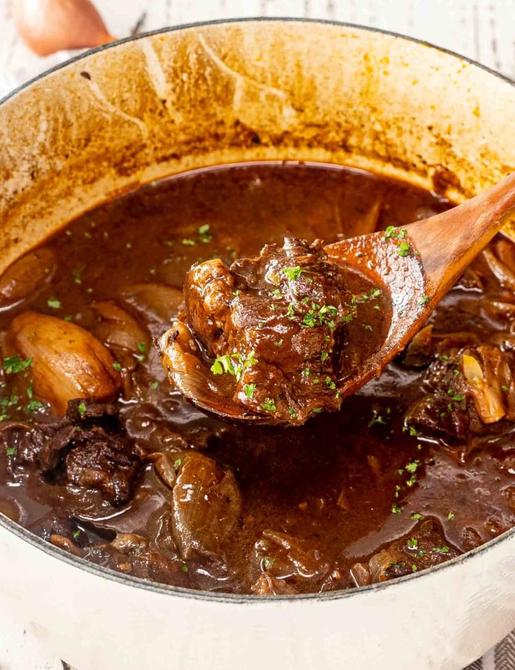 beef stifado (greek beef stew in a dutch oven with a wooden spoon inside.