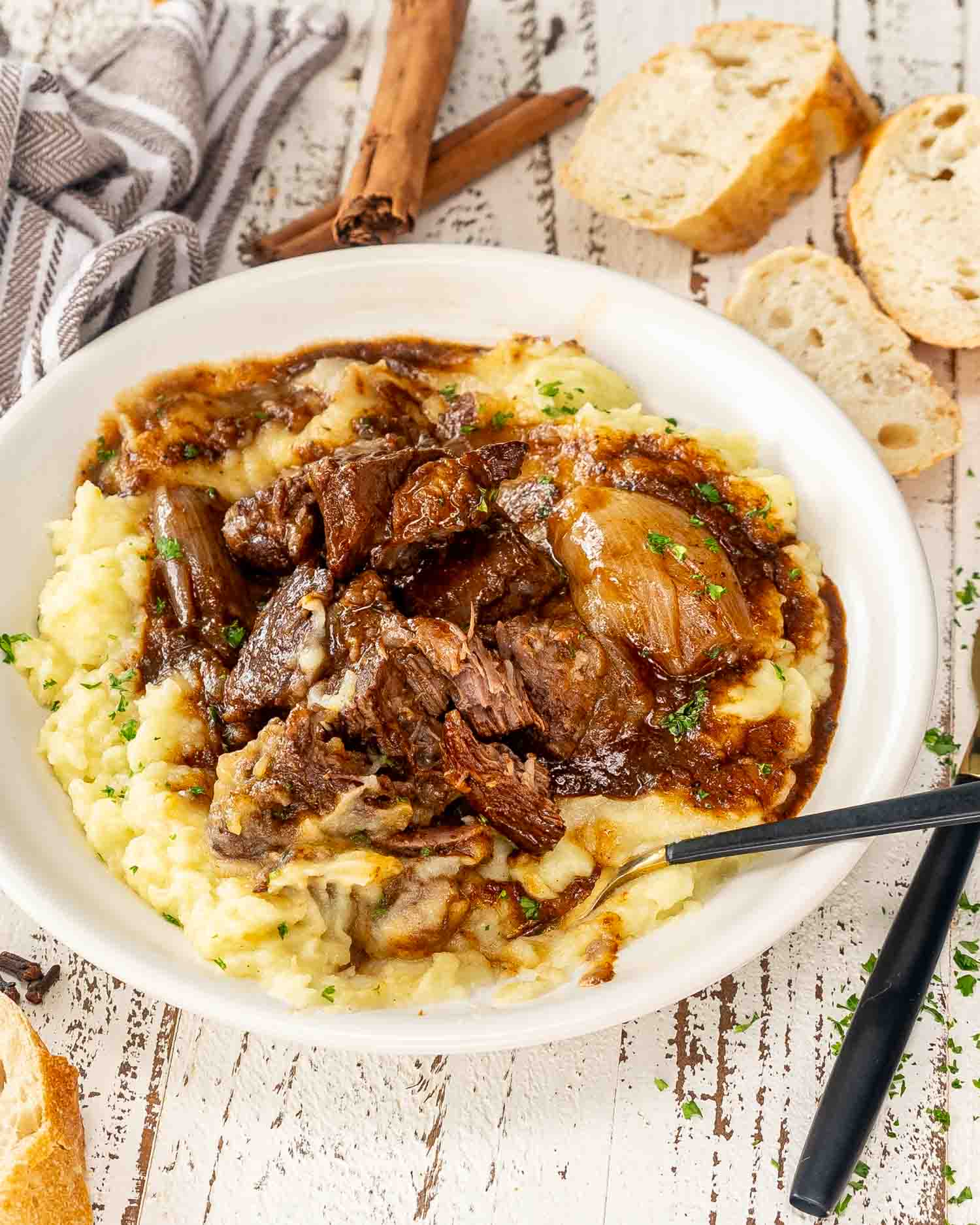 a serving of beef stifado over a bed of mashed potatoes.