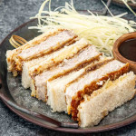 katsu sando on a metal plate with tonkatsu sauce in a bowl and cabbage.