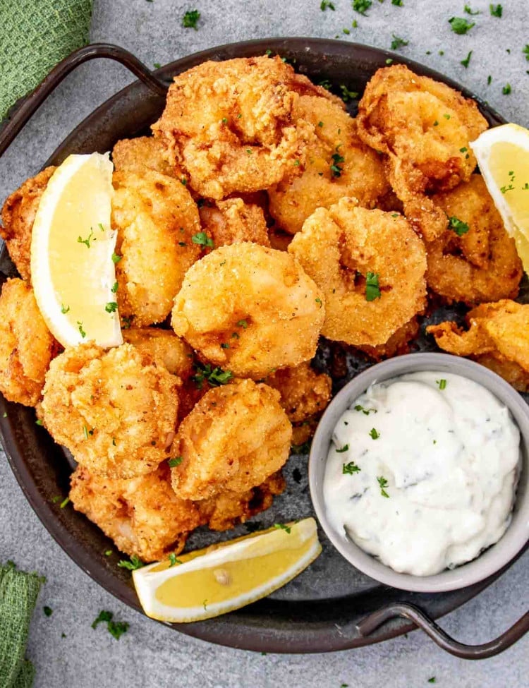 popcorn shrimp on a platter with a little bowl with tartar sauce and garnished with lemon wedges.