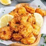 popcorn shrimp on a platter with a little bowl with tartar sauce and garnished with lemon wedges.