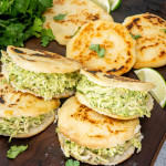 a few arepas on a cutting board stuffed with avocado chicken salad.