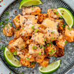air fryer bang bang salmon on a metal plate garnished with green onions and lime wedges.