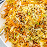 Colorful and vibrant Egg Roll in a Bowl served in a white dish, featuring ground pork, thinly sliced cabbage, shredded carrots, and garnished with sesame seeds and green onions.