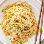 a serving of garlic noodles in a white bowl garnished with green onions.