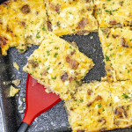 A slice of Amish Breakfast Casserole is being lifted from a baking dish with a red spatula.