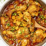 Pan of chicken afritada with tender chicken, potatoes, carrots, peas, and bell peppers in a rich tomato-based sauce.