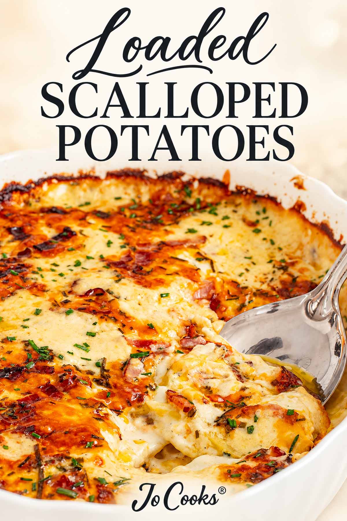 Loaded scalloped potatoes with golden melted cheese, bacon, and chives in a white casserole, with recipe title and Jo Cooks® logo.