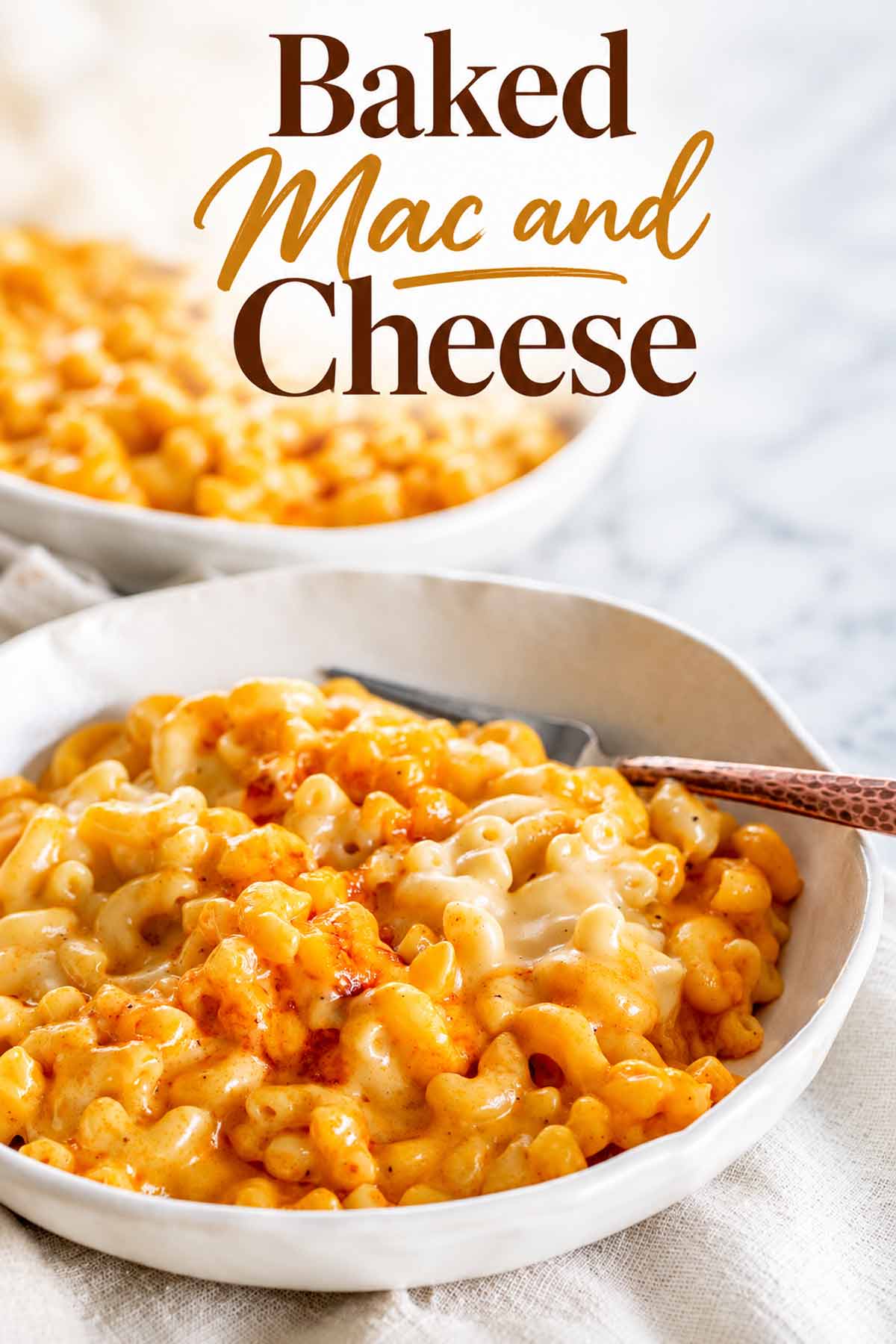Creamy baked mac and cheese served in a white bowl with a copper spoon and a second bowl behind it.