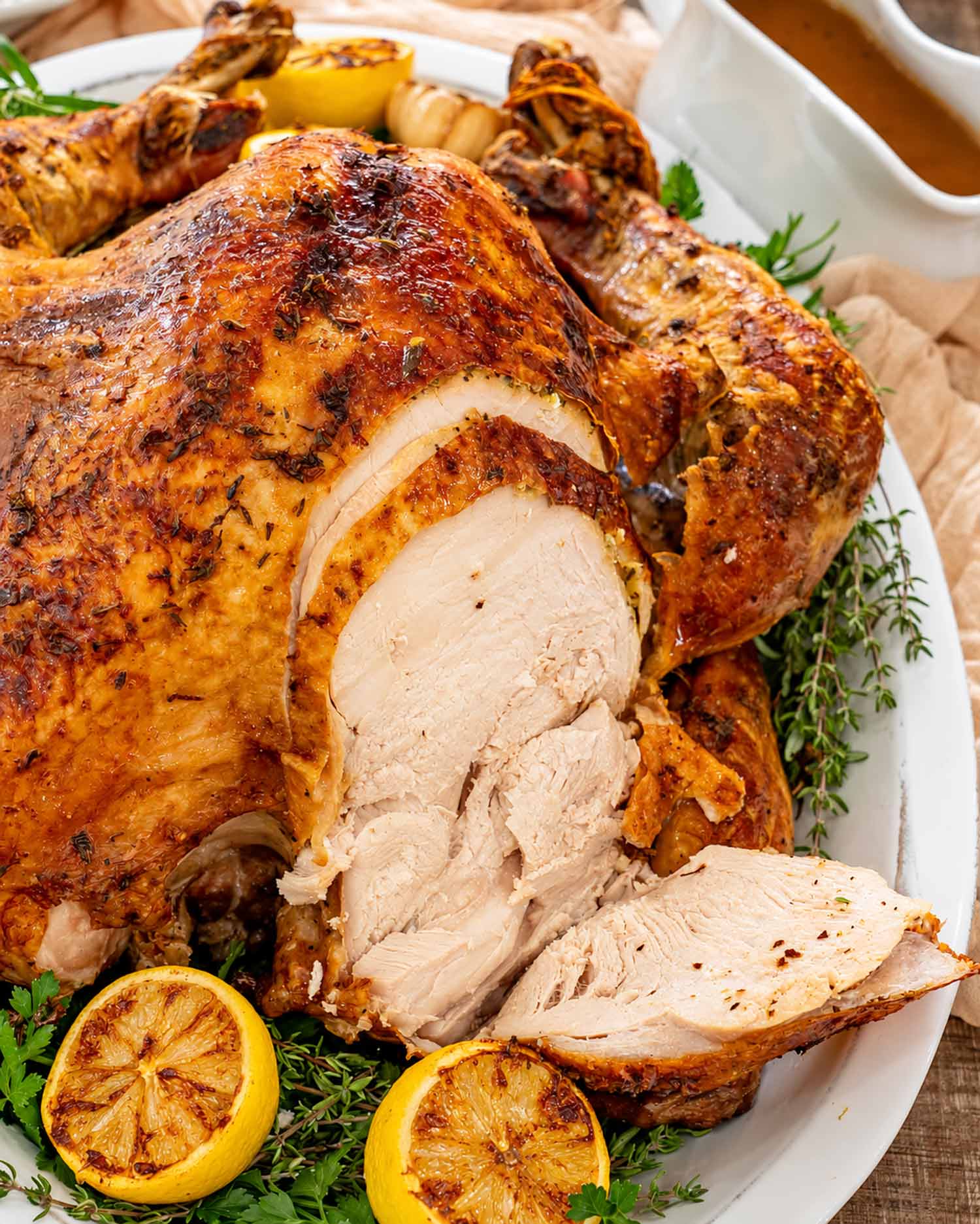 Partially carved roast turkey showing sliced white breast meat and golden skin, garnished with roasted lemons and fresh herbs.