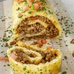 a beef potato roll on a cutting board cut into slices and garnished with parsley.
