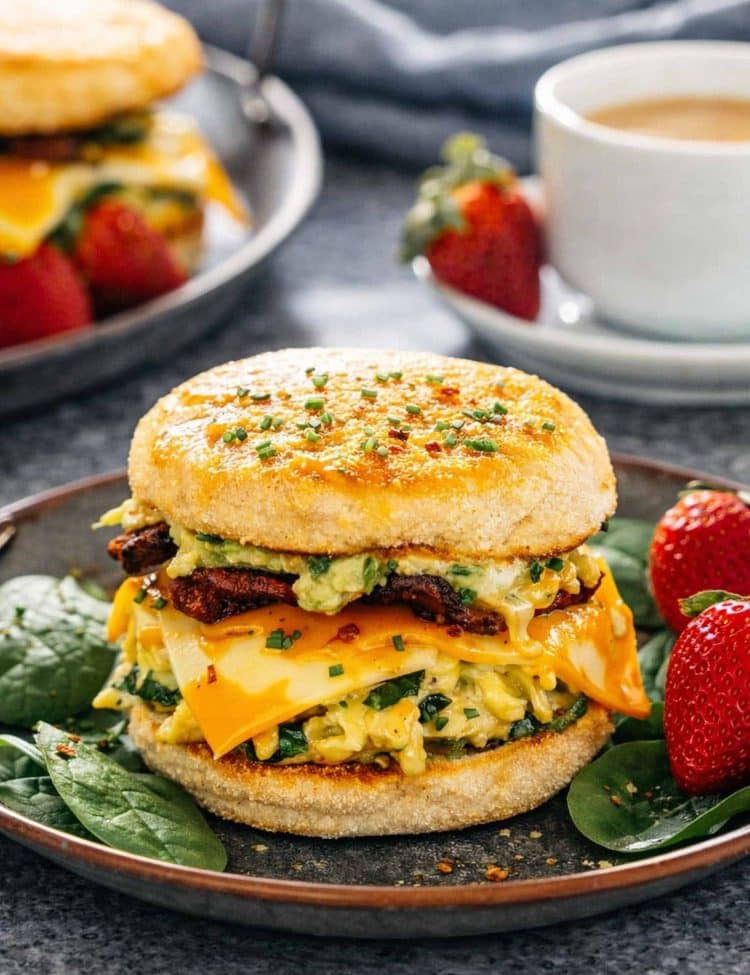 a breakfast sandwich on a metal plate with strawberries on the side.