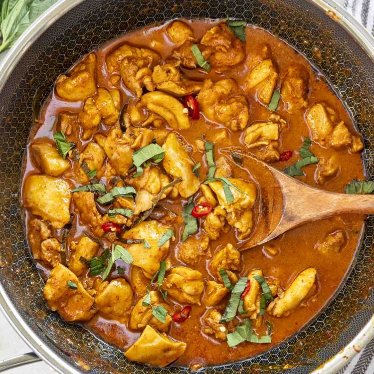 Panang Chicken Curry in a wok, featuring tender chicken pieces coated in a rich, aromatic curry sauce garnished with fresh basil and red chilies, ready to serve.