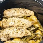 Close-up of slow-cooked chicken breasts, golden baby potatoes, and green beans, all seasoned with garlic, ranch, and butter, inside a black slow cooker.