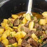 A slow cooker filled with tender beef chunks and golden potato pieces in a savory broth, ready to be served.