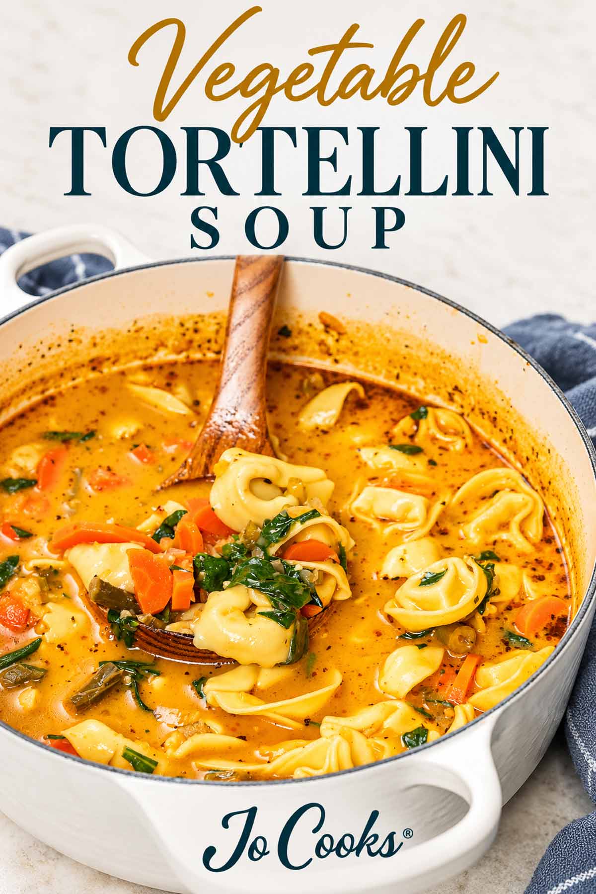 Wooden ladle holding tortellini, carrots and spinach above creamy soup in a white pot, with recipe title and Jo Cooks logo.