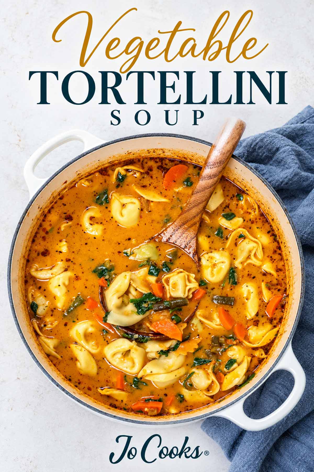 Overhead view of vegetable tortellini soup in a white Dutch oven with a wooden ladle, recipe title and Jo Cooks logo.