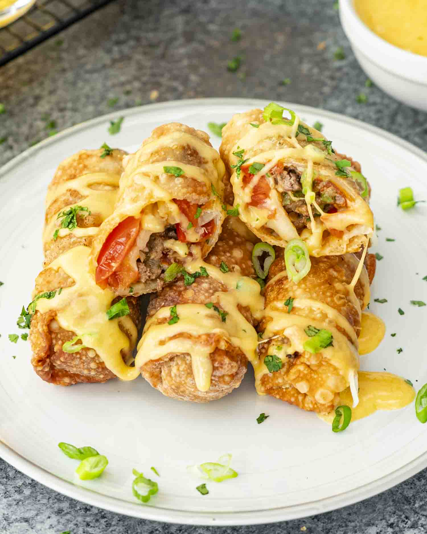 Golden, crispy beef taco egg rolls drizzled with creamy beer cheese sauce, garnished with fresh cilantro and green onions.