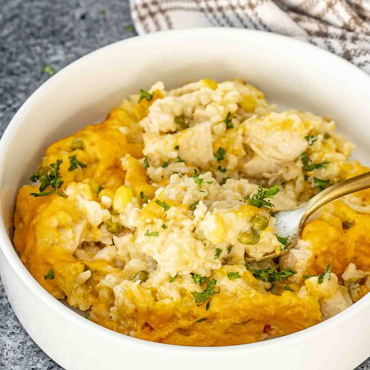 a serving of chicken and rice casserole in a white bowl with a golden fork inside.