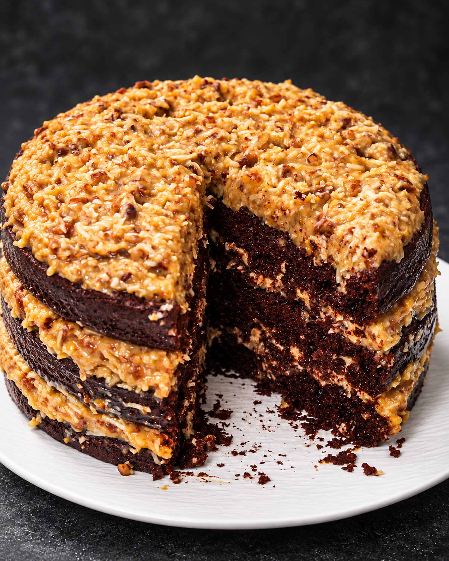 Three-layer German chocolate cake with a slice removed, showing dark chocolate layers and generous coconut pecan filling.