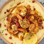 A bowl of creamy grits topped with juicy shrimp, crispy bacon, and fresh parsley, garnished with a lemon slice.