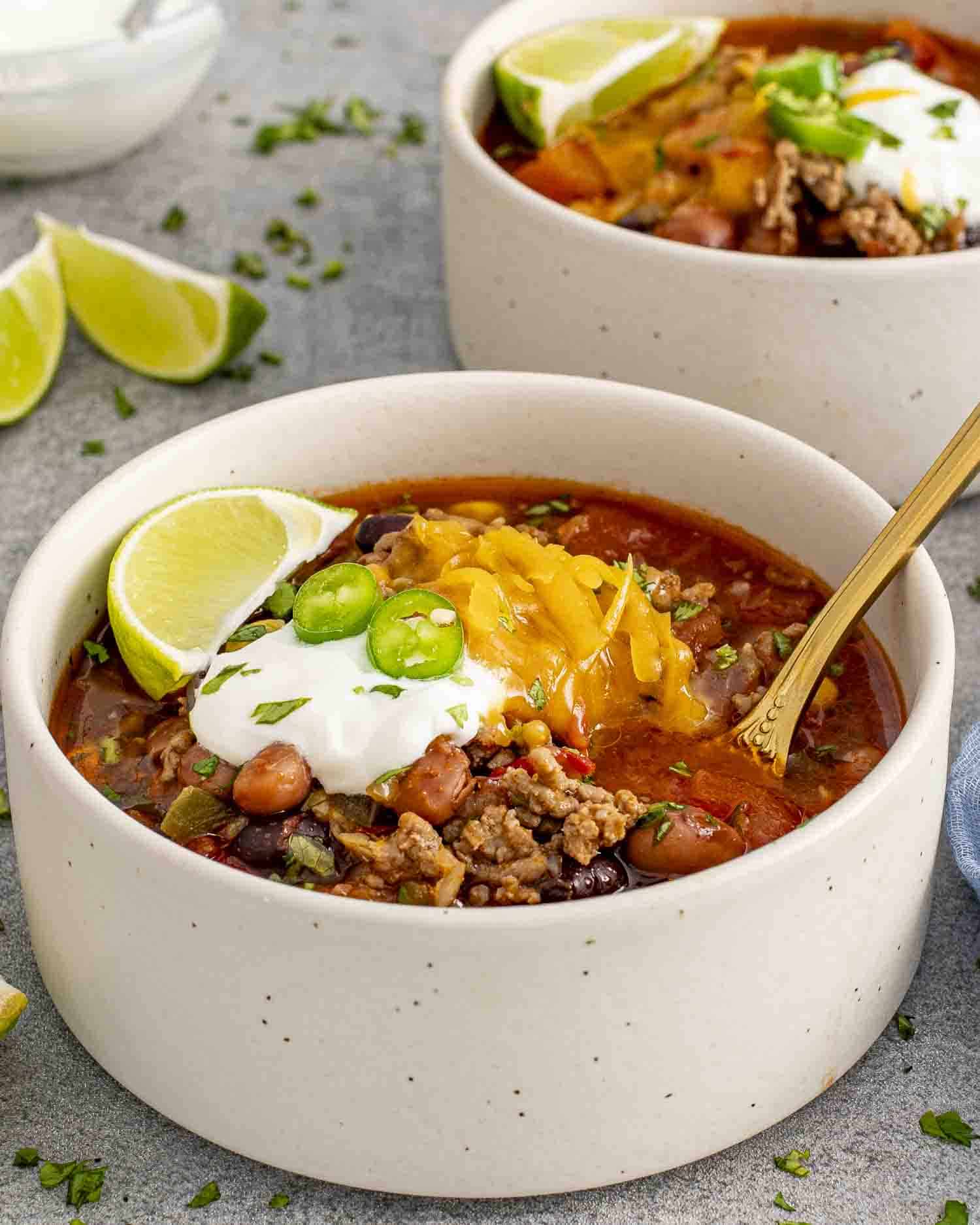 A bowl of taco soup topped with melted cheese, sour cream, sliced jalapeños, and fresh cilantro, served with a lime wedge on the side.