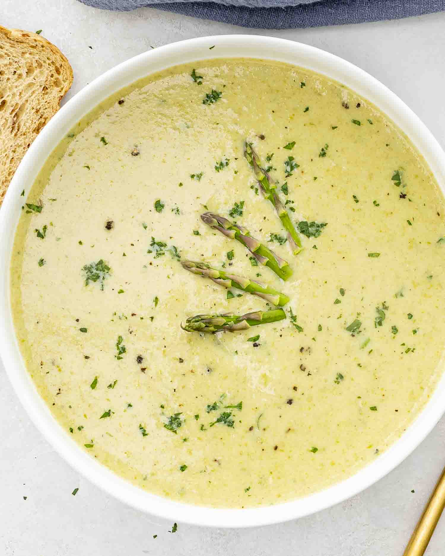a serving of asparagus soup in a white bowl garnished with fresh asparagus and parsley.