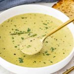 a serving of asparagus soup in a white bowl garnished with fresh asparagus and parsley.