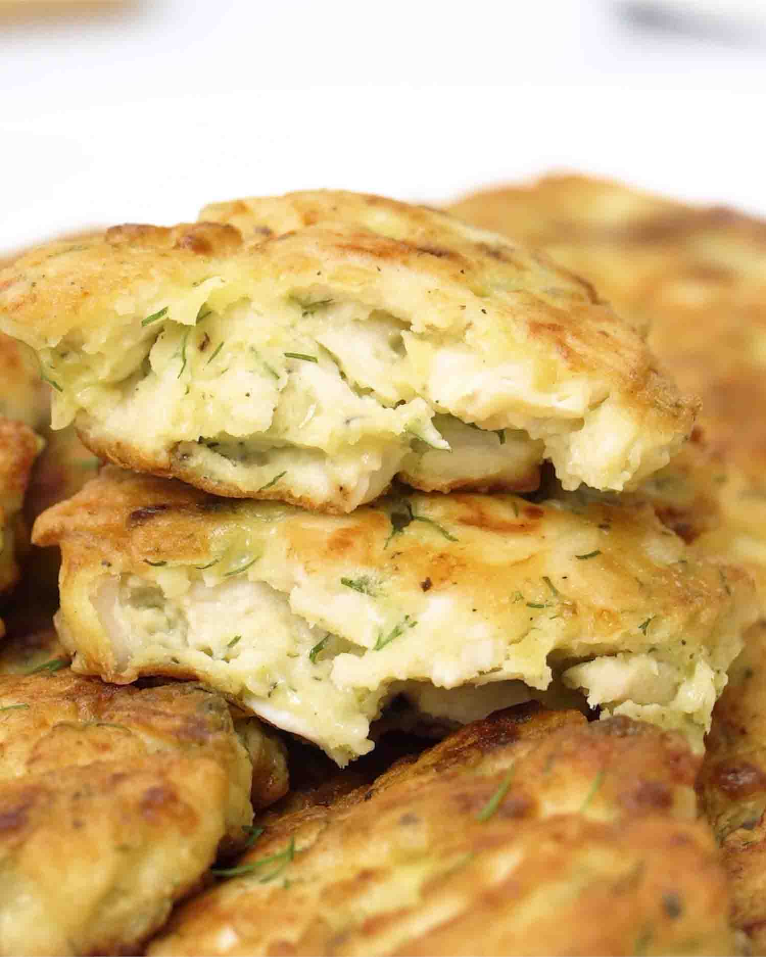 Close-up of a fluffy, golden chicken fritter torn open, showing its juicy, herby interior with fresh dill.