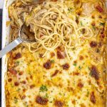 Cheesy chicken spaghetti casserole in a white baking dish, topped with golden melted cheese and garnished with chopped parsley.