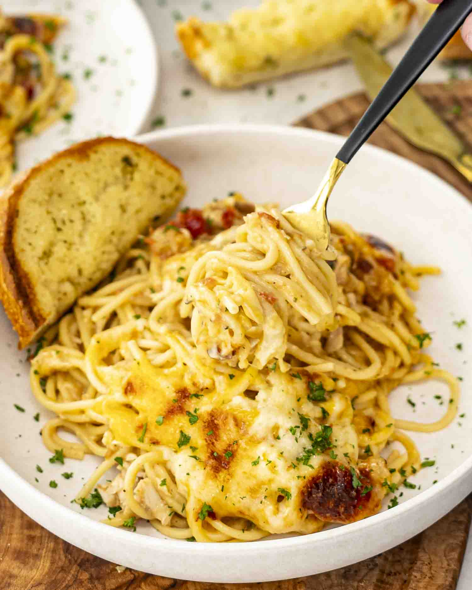 Cheesy chicken spaghetti twirled on a fork, served on a plate with garlic bread and sprinkled with fresh parsley.