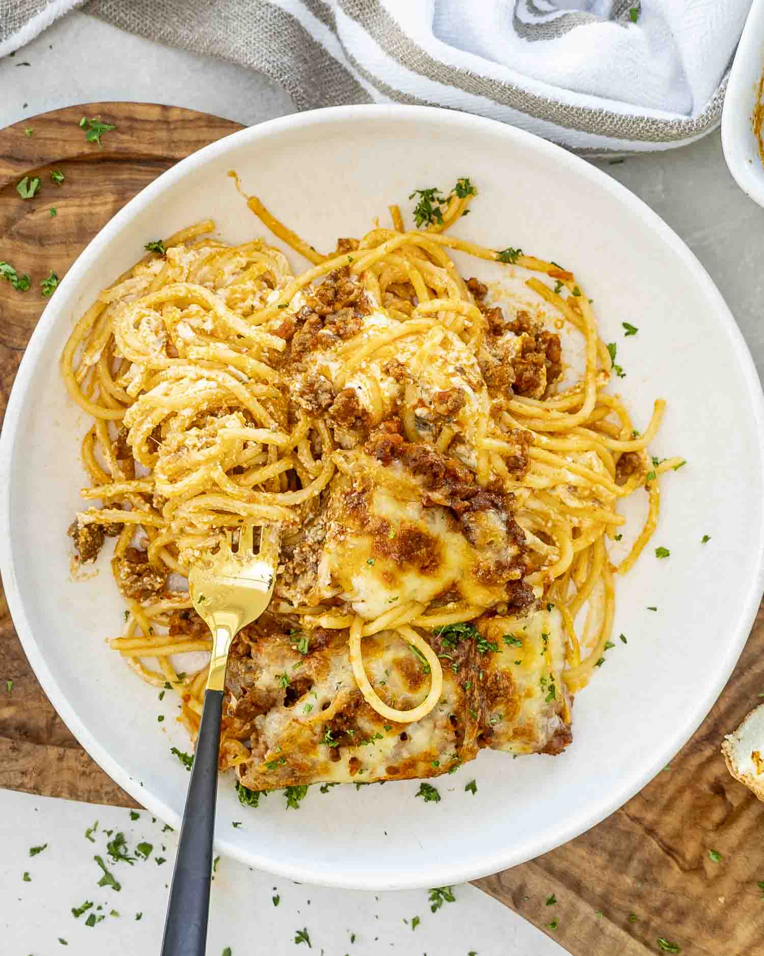 Plate of baked million dollar spaghetti with golden cheesy topping, twirled noodles, and sprinkled parsley, served with a gold fork.