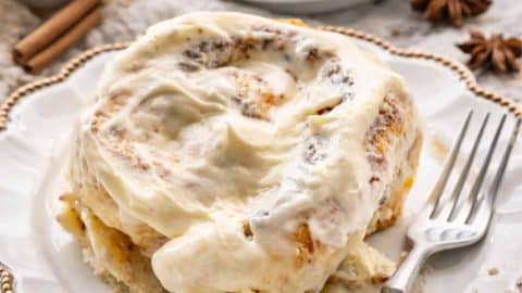 a cinnabon cinnamon roll on a white dessert plate with a cup of coffee in the background.