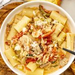Overhead shot of rigatoni pasta with creamy chicken, peppers, onions, and melted cheese in a white bowl.