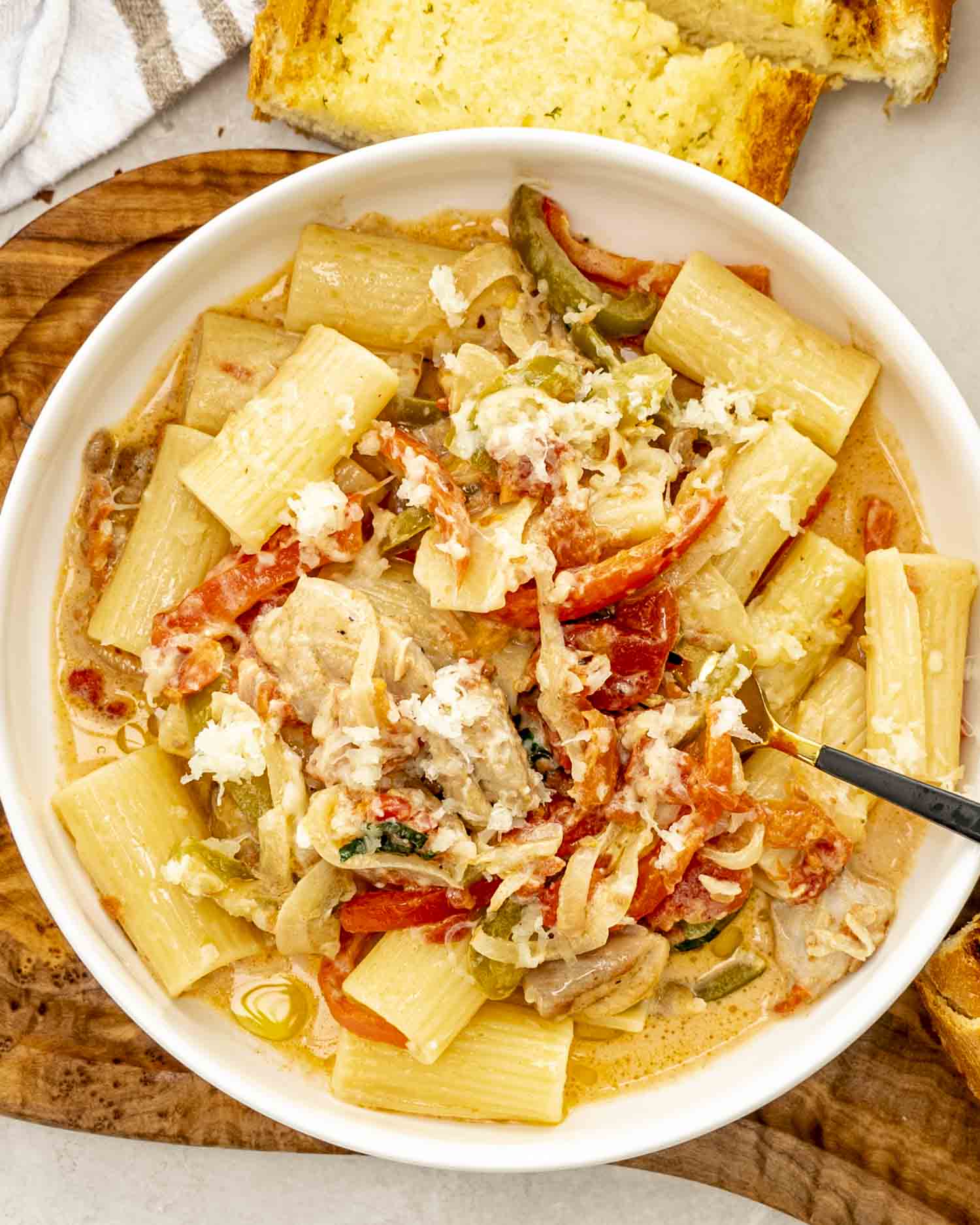 Overhead shot of rigatoni pasta with creamy chicken, peppers, onions, and melted cheese in a white bowl.
