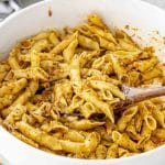 Large white bowl of pasta coated in tomato-almond pesto, with a wooden spoon mid-toss.