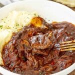 Tender steak smothered in tomato sauce served with mashed potatoes in a white bowl with fresh parsley.