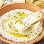 Bread slice dipped into creamy white bean dip, coated generously, with grated cheese and olive oil swirl.